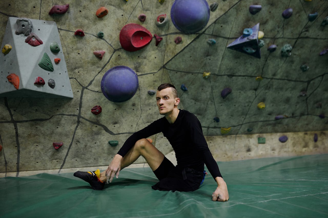 Male adaptive climber sitting on an indoor climbing mat, surrounded by colorful holds.
