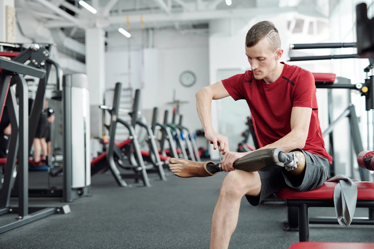 Amputee athlete adjusts prosthetic leg in the gym, showcasing determination and fitness.