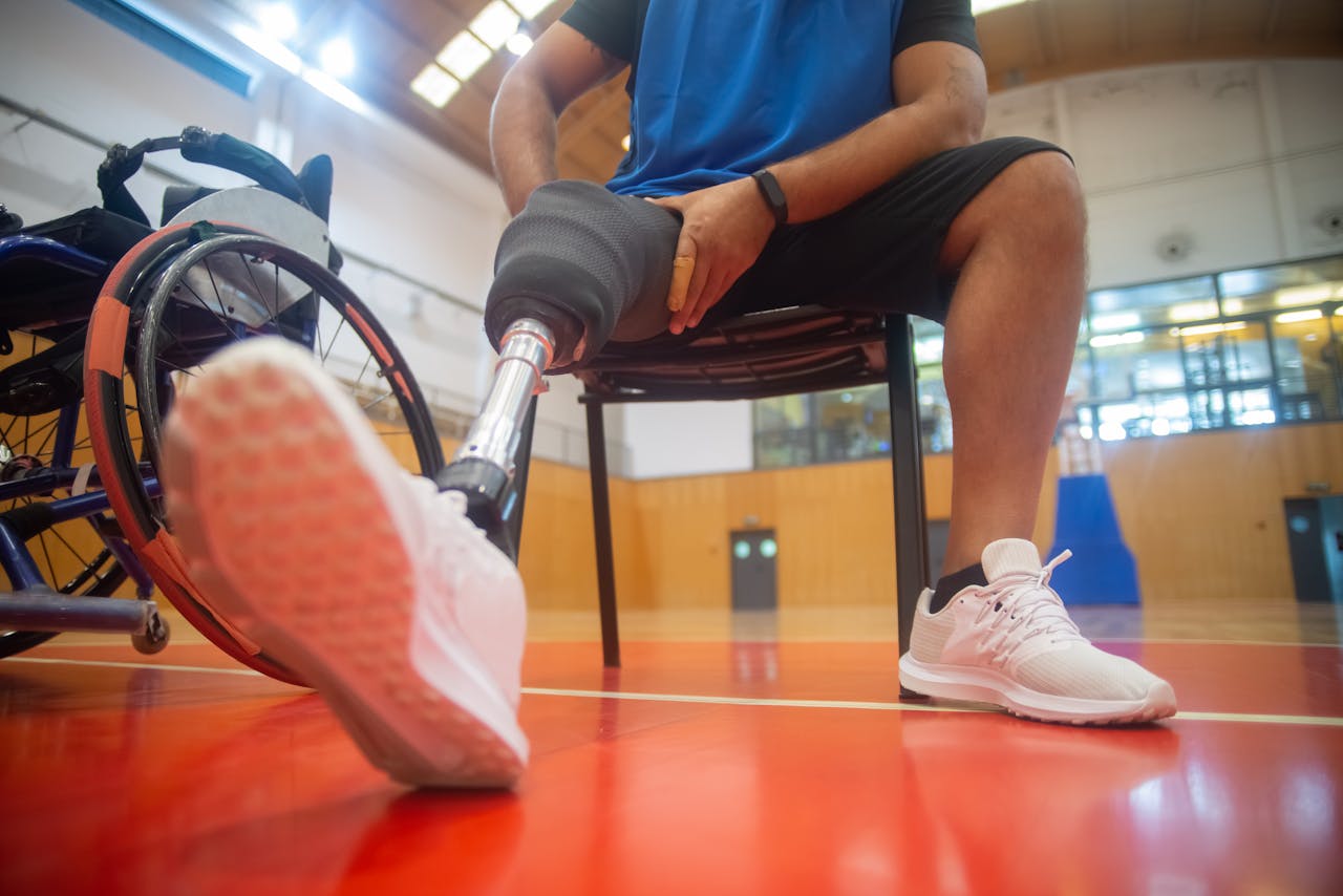 An amputee with a prosthetic leg sitting on a basketball court next to a wheelchair, showcasing adaptive sports.